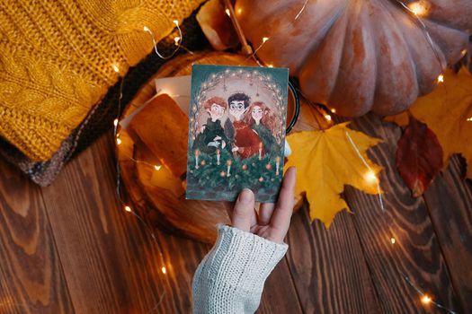 Postcard with illustration from Harry Potter in hand. Pumpkin, knitted sweater, autumn leaves and lights of garlands on a wooden background. Golden trio. Bishkek, Kyrgyzstan - November 1, 2019.