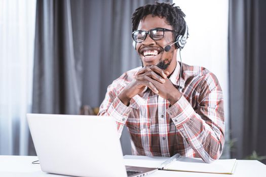 Happy freelancer or African american student working at home using laptop with head phones for a group video call working distantly. Young Student on distant leaning have a video group call.