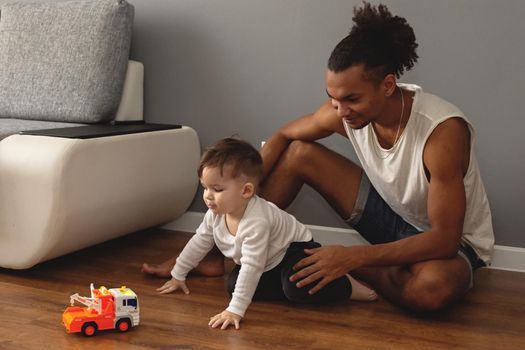 Young father and little son play on the floor of the room. Copy space