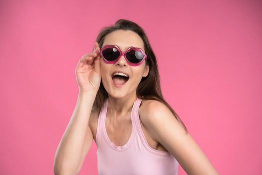 Suffering of headache or migraine young woman in sleeveless pink t-shirt holding her head with eyes shut isolated on pink background. Stressed employee woman in stripe suit. With copy space.