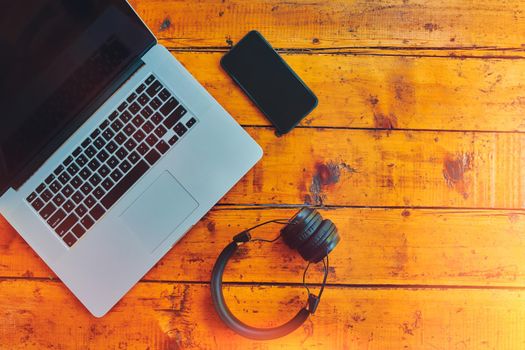 Laptop, wireless headphones and smartphone on wooden table. Freelancer's work surface. Modern devices for business podcast and entertainment. Top view with copy space.