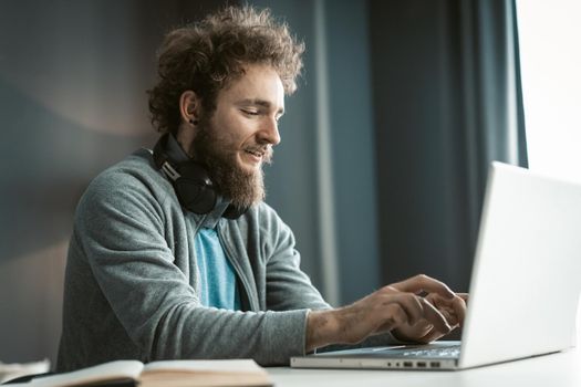Young freelancer man working at laptop sitting at the desk at home office and making notes or programming as IT specialist. Remote working handsome young man working at home. Work from home concept.