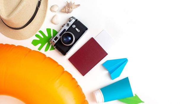 Summer travel set top view: orange swimming circle, passport, camera, straw hat, sun cream lies on white background. Copy space. Wide