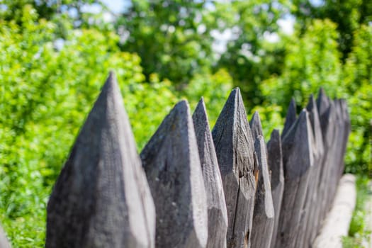 Fence made from sharp wooden stakes. Close-up on an old fence made of stakes, a picket fence, a protective structure near an old wooden fortress, selective focus