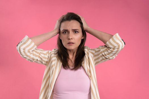 Suffering of headache or migraine young woman in sleeveless pink t-shirt holding her head with eyes shut isolated on pink background. Stressed employee woman in stripe suit. With copy space.