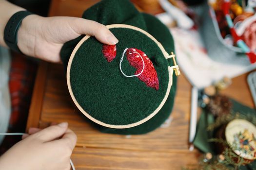 Girl's hands embroidery fly agaric hat on frame. Wooden table with different objects on background. Concept of hobbies needlework and crafts.