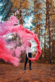 Smoke screen in the woods. Woman with smoke. Beautiful woman with pink smoke behind her in the forest