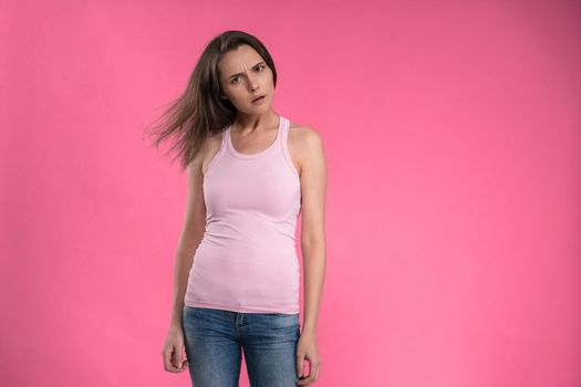 Suffering of headache or migraine young woman in sleeveless pink t-shirt holding her head with eyes shut isolated on pink background. Stressed employee woman in stripe suit. With copy space.