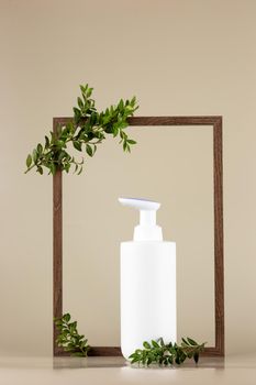 White cosmetic bottle, stands in an empty wooden frame with branches of a green plant, on a beige background. Mock up