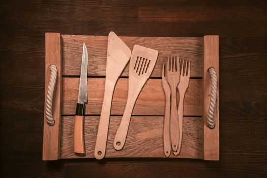 Wooden kitchen utensils laid out on wooden tray on wooden table horizontal banner. Top view.