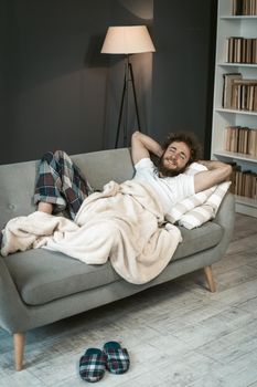 Portrait of relaxed handsome curly hair man sleeping on the couch or sofa, enjoying weekend or quarantine days at home with small home library on background.