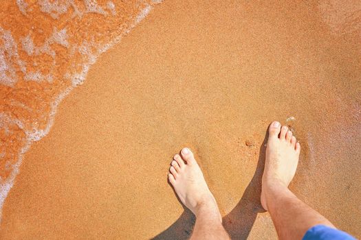 Bare male feet on seashore. Walk along ocean beach. Summer holidays. Travel and tours to hot countries. A wave washes the shore. Empty copy space.