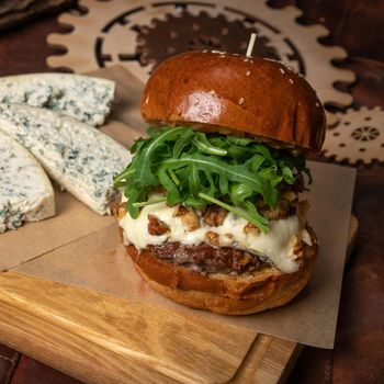 Fresh craft beef burger with fresh arugula salad and, fresh blue cheese slices laying next to it. Restaurant concept. Street food concept.