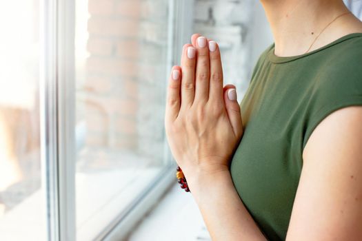 Girls in a green T-shirt, in a yoga pose close-up, folded their palms together on their chest, close-up, stands by the window in the daylight. No face
