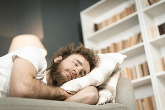Sleeping on the sofa handsome bearded young man hugging a pillow after a long hours working late nigh. Sick young man sleeping on the couch after taking medications. distance work concept.