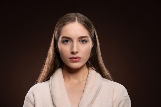 Standing in a bath robe natural beauty girl with no make up face. Healthy pure skin model posing on camera isolated on dark background. Natural make up concept. Spa and beautiful concept.
