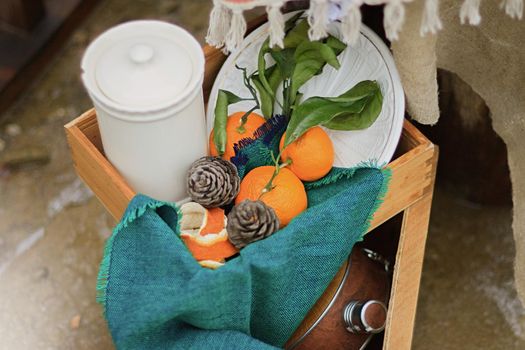 Tangerines with leaves, lie in a woods box with a blue napkin and a white jar with a lid and white plate