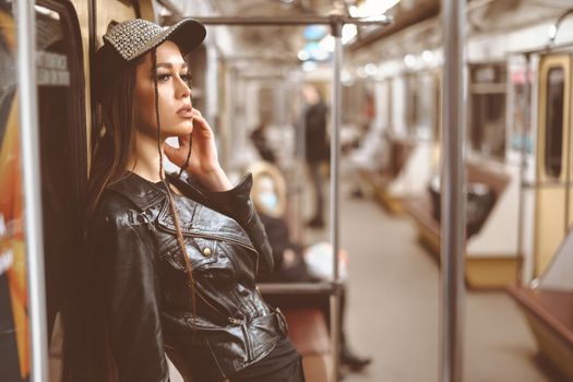 Pretty Caucasian Woman in Leather Jacket and Stylish Cap Leaning Back against the Underground Train Door. Beautiful Face. Close-up Portrait. Toned picture. High quality photo