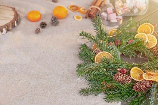 Rustic Christmas table with natural spruce wreath, dried oranges, fresh tangerines, pine cones on a fabric tablecloth. Copy space