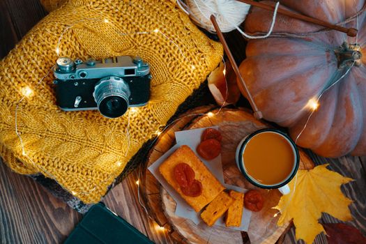 Flat lay of the autumn composition. The concept of Thanksgiving. Tea, pumpkin, freshly baked pie, dried apricots on a wooden tray. Orange sweater, a vintage camera, a garland and fall yellow leaves.