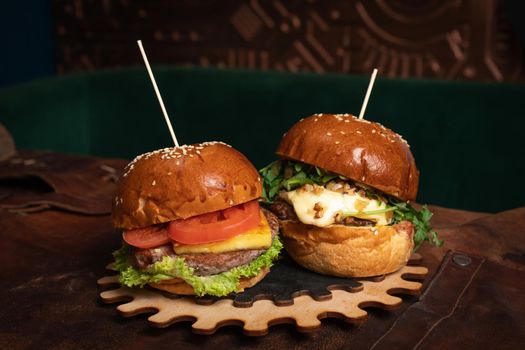 A double serving of fresh beef burgers and one with fried walnuts are served on a decorative wooden part of a simple mechanism. Restaurant concept. Fast food concept. Street food concept.