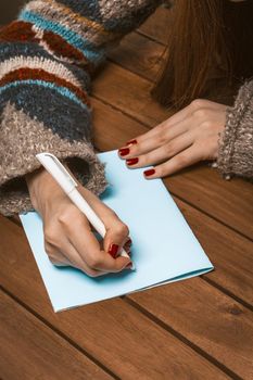 Woman Hands with Red Manicure on a Wooden Table Write a Greeting Card with a Pen. Woman Fill in a Letter on a Piece of Blue Paper. Blank Sheet. Close-up. High quality photo