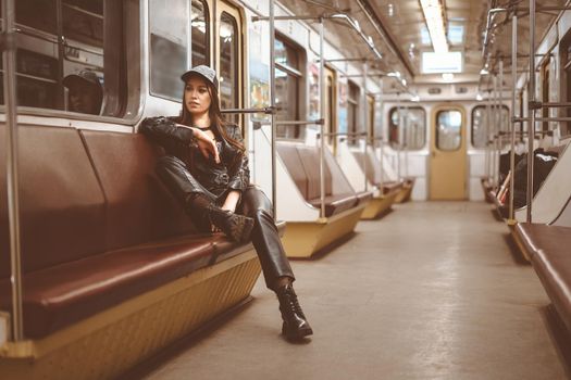 brutal woman in a leather jacket, leather pants and ankle boots sits alone in a train car. Toned picture. Close-up. High quality photo