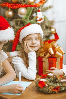 Little Sisters Girls in Christmas Hats Write a Letter to Santa Claus and Enjoy Christmas Eve. High quality photo