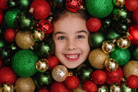 Cheerful portrait of a little girl in red, green and gold Christmas balls.