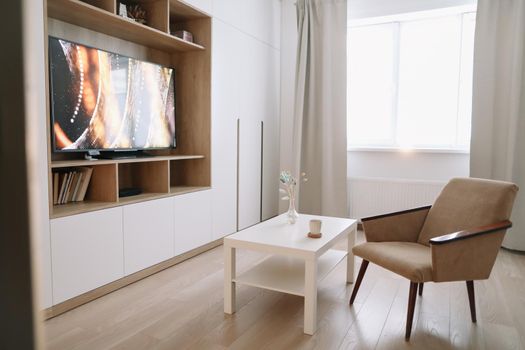 Stylish modern living room interior design with TV, armchair, coffee table and a window with curtains. Minimalistic apartment for rent. 