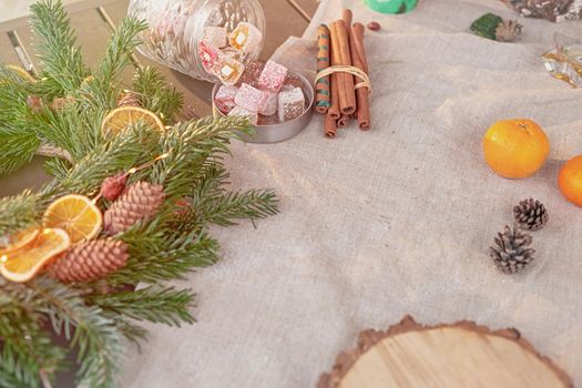 Rustic New Year's table with a natural spruce wreath, dried oranges, fresh tangerines, pine cones and a round saw cut made of wood on a fabric tablecloth. Copy space