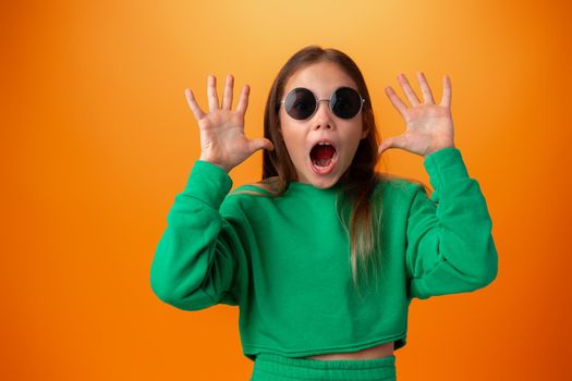 Funny caucasian teen girl in eyeglasses isolated on orange background, close up