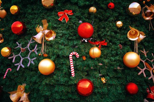 New Year atmosphere and pine decorations. Christmas tree with festive ornaments. Ribbon, snowflake, red bells and balls on green fir branches. Background for postcards and posters. Winter holidays.
