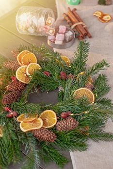 natural spruce wreath, dried oranges, fresh tangerines, pine cones, cinnamon sprigs and sweets on a fabric tablecloth. Copy space. Vertical