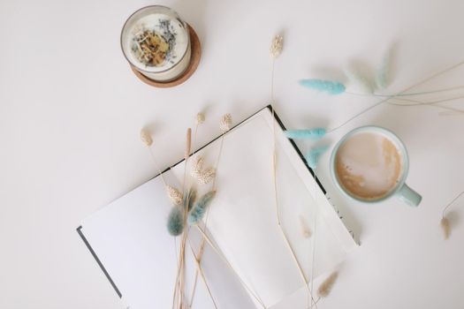 Blank paper sheet, coffee cup and dry flowers on white background. Minimal home workspace desk table. Flat lay, top view, mockup with copy space 