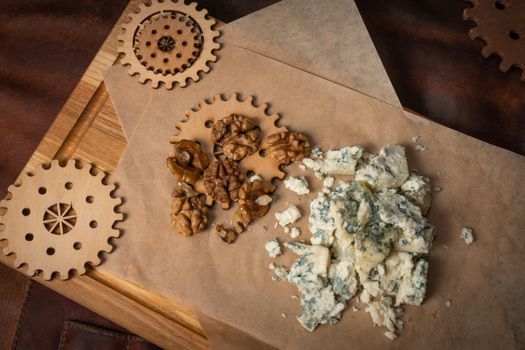 Top view of a blue cheese or bleu cheese served with walnuts on food wrapping paper and chalkboard with decorative wooden details of a simple mechanism. Cheese with the mold.