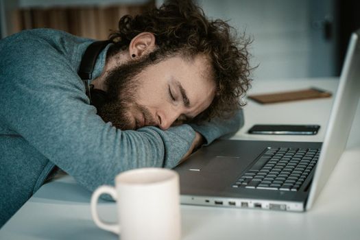 Man With Folded Hands Sleeps on Desk With Laptop. Sleep Sitting, Freelance at Night, Coffee Mug on the Table. Close-up. High quality photo