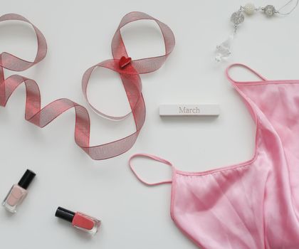 Concept Women's Day, March 8. Female underwear with a red ribbon and cosmetics on white background. Styled flat lay, top view, copy space