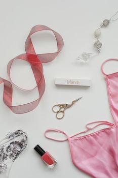 Flat lay composition of female underwear with a red ribbon and cosmetics on white background. Styled flat lay, top view, copy space. Concept Women's Day, March 8. 