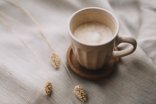 Cup of coffee with milk on beige textile. Still life morning breakfast concept. Warm and comfortable atmosphere Photo in light pastel colors. 