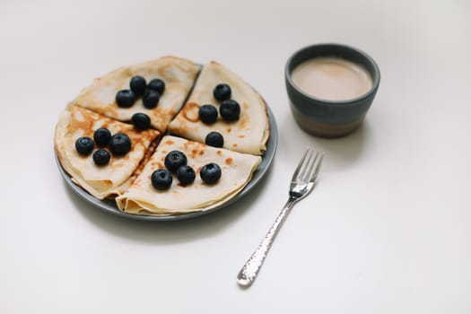 Pancakes with blueberries on a white table with a coffee cup