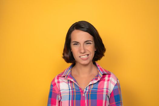 Emotional denial or hesitation charming brunette looking to camera. Young woman in a plaid shirt on yellow background. Human emotions, facial expression concept.