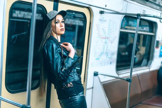 sexy woman in stylish clothes with long brown hair stands by back at the door in a train car. glamorous female in empty Underground Train. Close-up. High quality photo