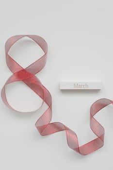 Red ribbon and word MARCH on white background. 8 March, International Women's Day, spring and love concept. Flat lay, top view, copy space, mockup, web site header, advertising banner.