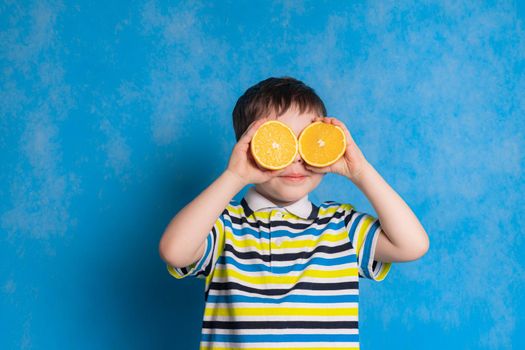 A boy with an orange on a blue background . An article about baby food. Baby vitamins. Copy space. A boy on a blue background