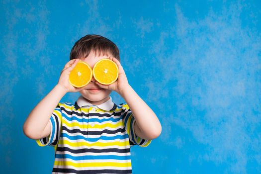 A boy with an orange on a blue background . An article about baby food. Baby vitamins. Copy space. A boy on a blue background