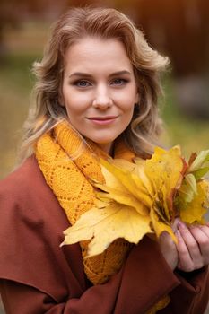 Beautiful young woman posing for camera with autumn leaves in hand and fall yellow garden or park. Beautiful smiling young woman in autumn leaves.