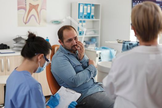 Specialist orthodontist team explaining oral hygiene to patient with toothache discussing medical expertise during stomatological consultation in dental office. Concept of medicine service