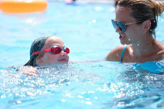 Woman coach teaching swimming to little girl in pool. Swimming lessons for children concept