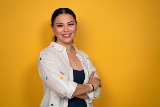 Facial expressions, feelings. Pleasant looking glad Asian woman looks in camera, has toothy smile, wears casual clothing, isolated on yellow background. Human emotions, facial expression concept.